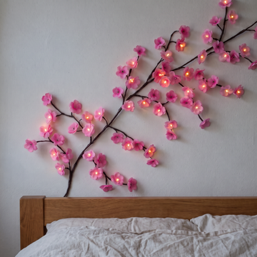 Pink Hanari cherry blossom vine lights glowing above a headboard at dusk